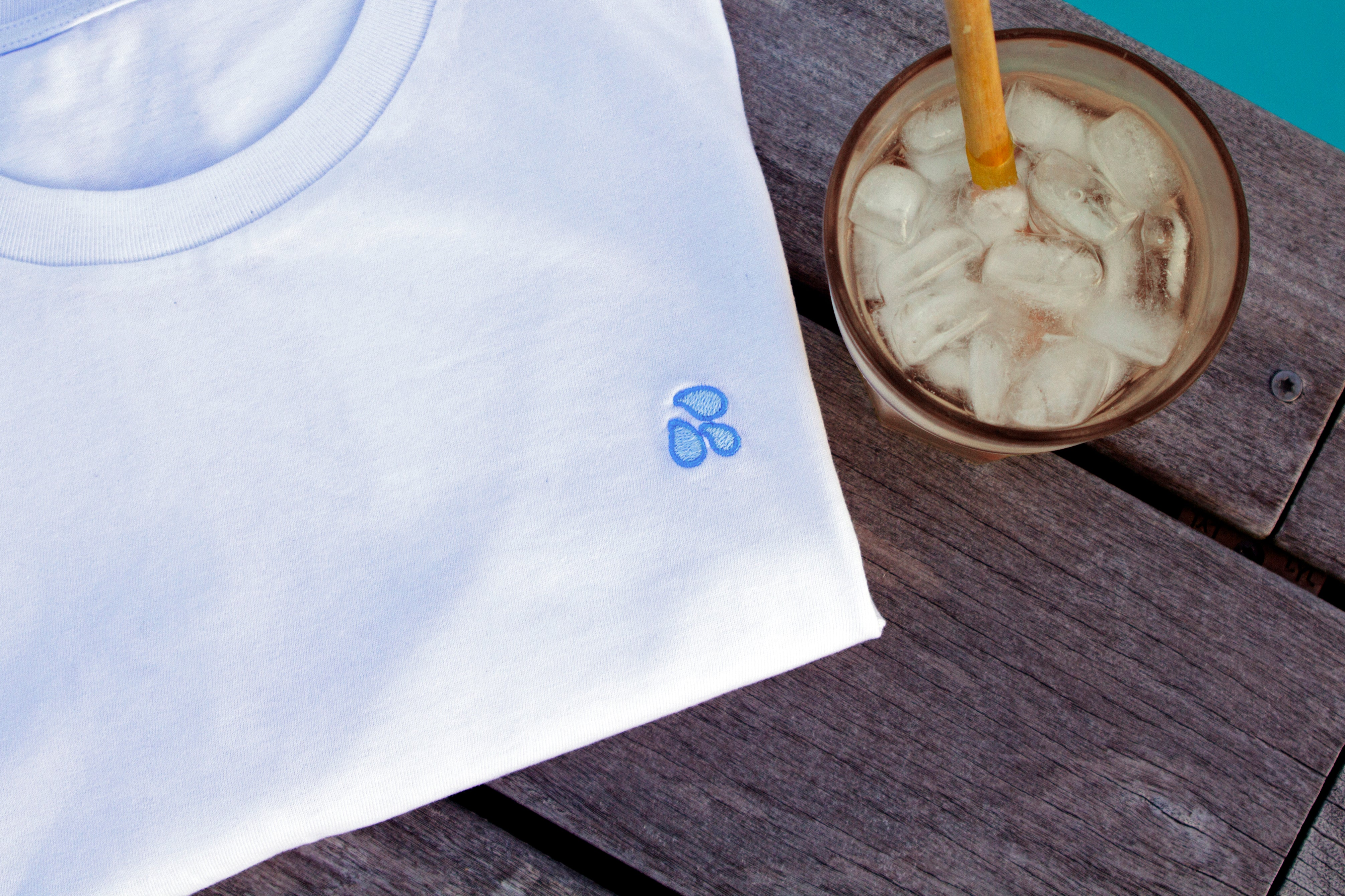 White t-shirt with drops design by Out Now! folded neatly in a stylish setting, perfect for LGBTQ+ pride and icebreakers.