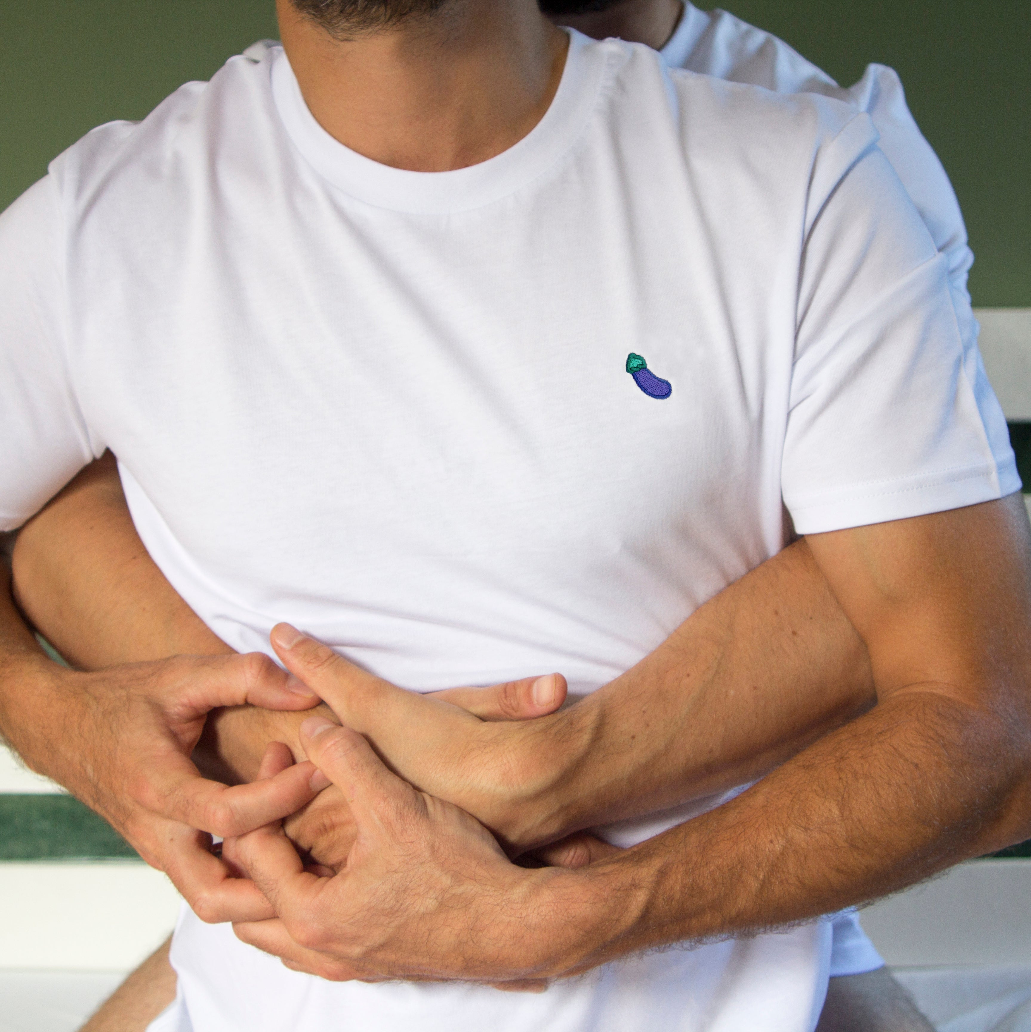 Out Now! eggplant-patterned t-shirt worn by a model while hugging a partner, symbolizing connection within the LGBTQ+ community.