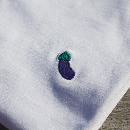 Zoomed-in detail of the eggplant pattern on a folded Out Now! white t-shirt.