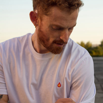 Model wearing Out Now!'s white t-shirt featuring a flame design, ideal as a conversation starter for the LGBTQ+ community.