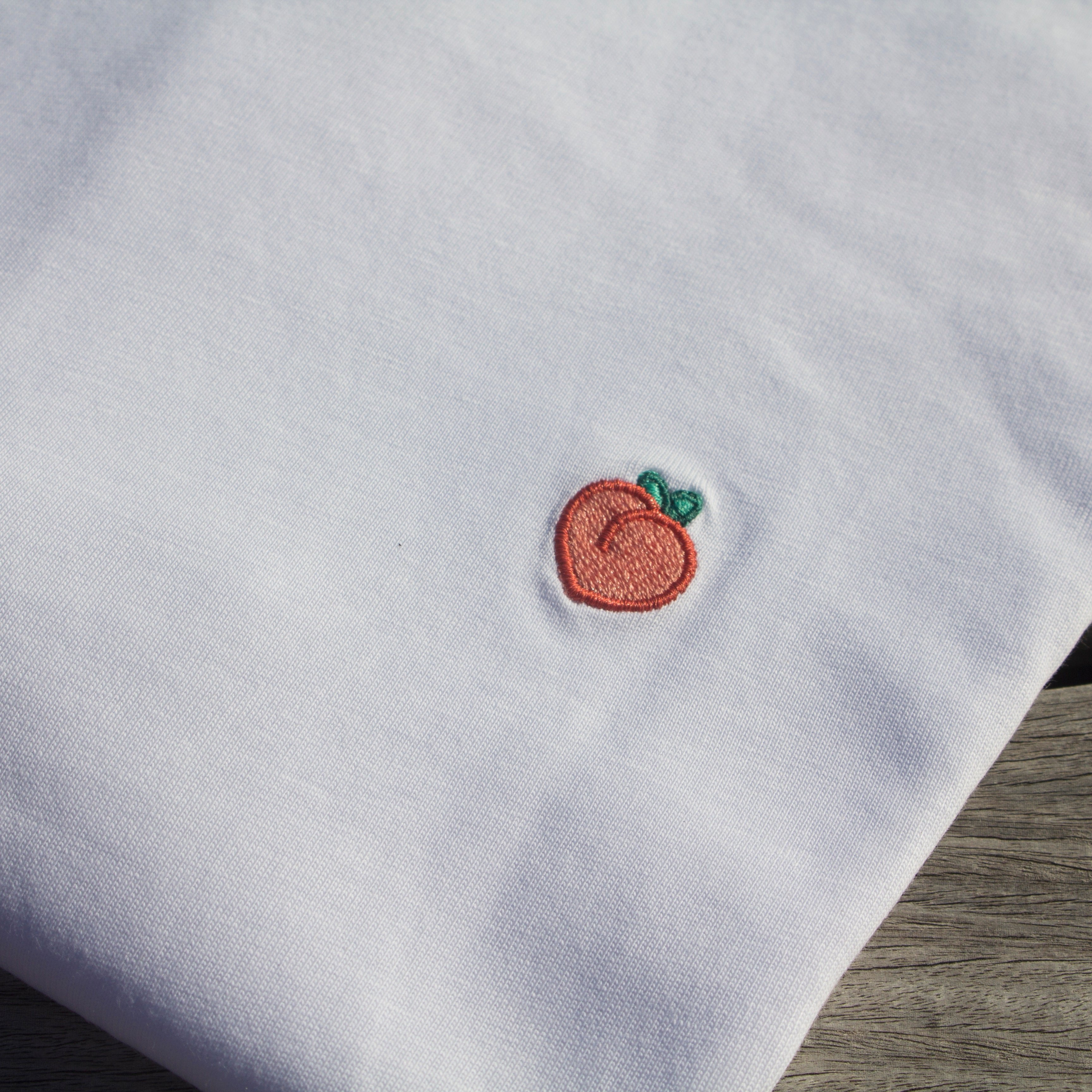 Zoomed-in detail of the peach pattern on a folded Out Now! white t-shirt.