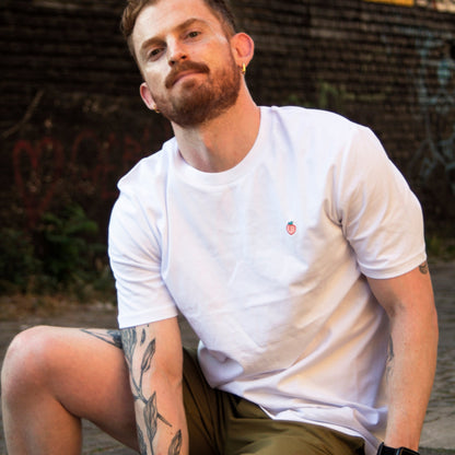 Model in a cheeky pose wearing Out Now!'s white t-shirt with a peach design, perfect as a playful conversation starter for the LGBTQ+ community.