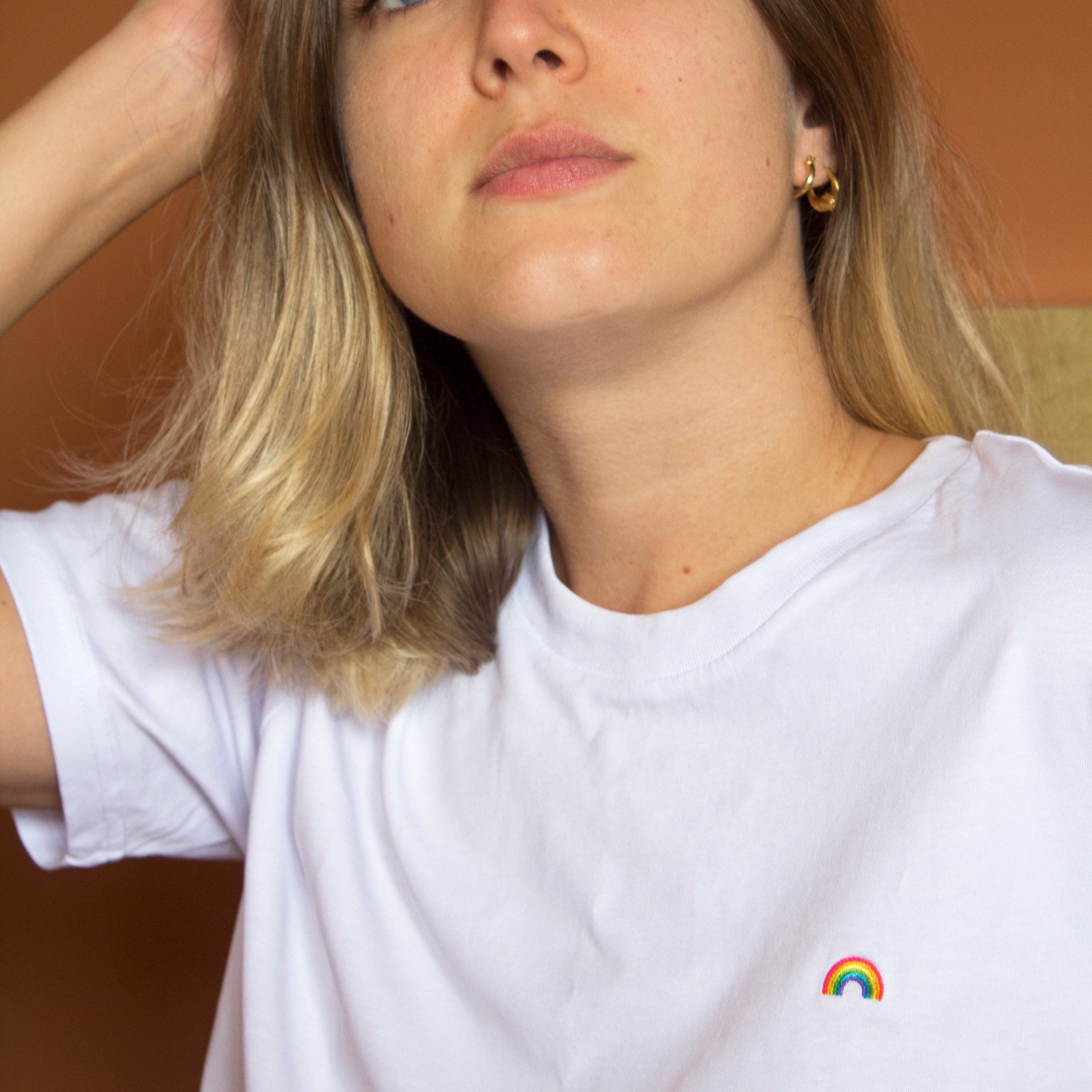 Out Now! female model wearing a white t-shirt with a rainbow pattern, designed as an icebreaker for the LGBTQ+ community.