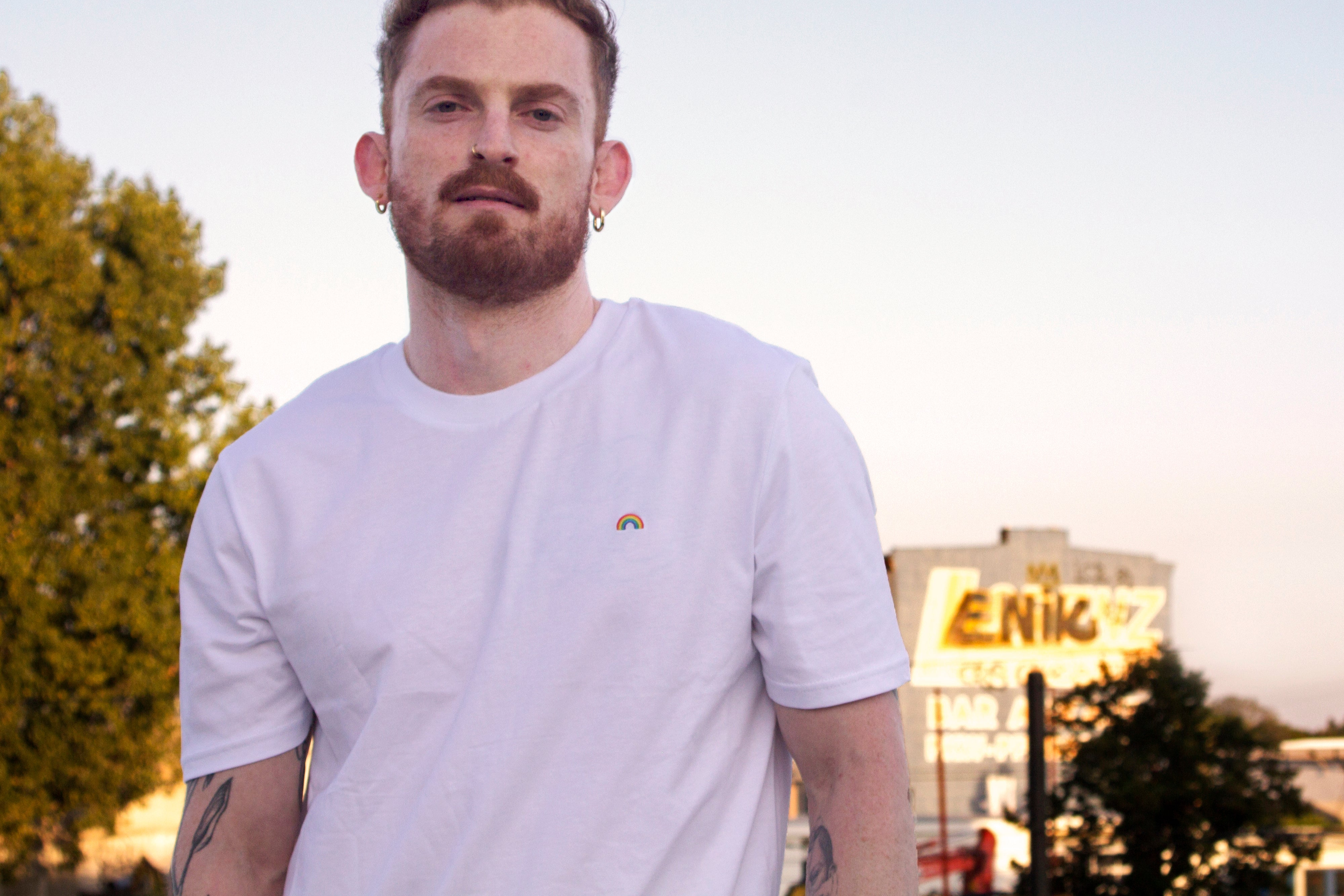 Out Now! male model wearing a white t-shirt with a rainbow pattern, designed as an icebreaker for the LGBTQ+ community.