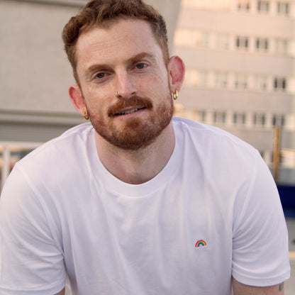 Model wearing Out Now!'s white t-shirt featuring a rainbow design, ideal for LGBTQ+ icebreakers.