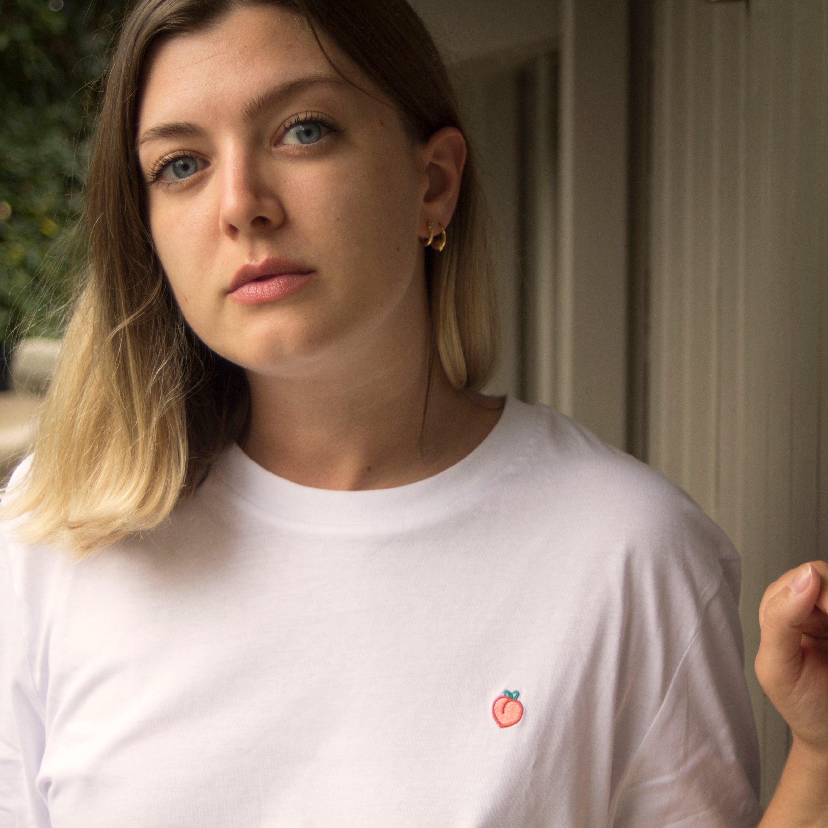 Out Now! female model wearing a white t-shirt with a peach pattern, designed as an icebreaker for the LGBTQ+ community.